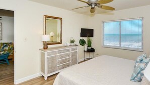 A bedroom with a bed, a ceiling fan, a dresser, a TV, and a window with blinds. - Your Slice of Gulf-Front Paradise (Sarasota)