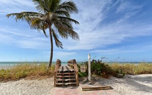 A wooden staircase leading to a beach with a palm tree and a signpost. - Unobstructed Panoramic Gulf Views & Steps to the Shoreline (Sarasota)