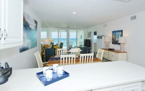 A spacious living area with a large dining table, white cabinets, and a view of the ocean. - Unobstructed Panoramic Gulf Views & Steps to the Shoreline (Sarasota)