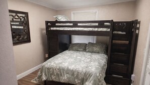 Een stapelbed met een bloemenprint sprei, een klein raam met zonwering en een decoratieve spiegel aan de muur.