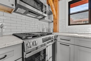 A modern kitchen with a stainless steel stove, white tiled backsplash, and wooden beams. - Ruby Cabin at Highland Peaks Retreat (Highlands)