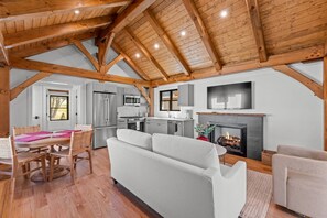 A spacious loft with a high ceiling, exposed wooden beams, a kitchen with modern appliances, a fireplace, and a dining area with a table and chairs. - Ruby Cabin at Highland Peaks Retreat (Highlands)