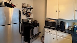 Una cocina compacta con un refrigerador de acero inoxidable, una estufa negra y gabinetes blancos.