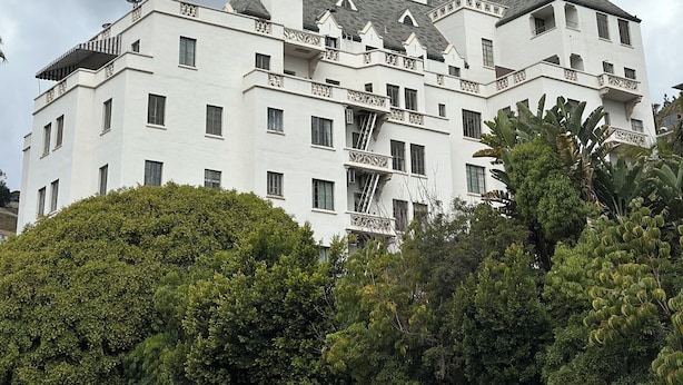 Un edificio grande y blanco con múltiples balcones y una torre, rodeado de exuberante vegetación.