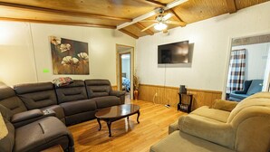 A living room with a sectional sofa, a coffee table, and a television mounted on the wall. - Peaceful Cabin in New Concord, KY on Kentucky Lake at Missing Hill Resort (New Concord)