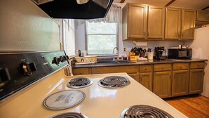 A kitchen with a white stove, wooden cabinets, a microwave, and a window with blinds. - Peaceful Cabin in New Concord, KY on Kentucky Lake at Missing Hill Resort (New Concord)