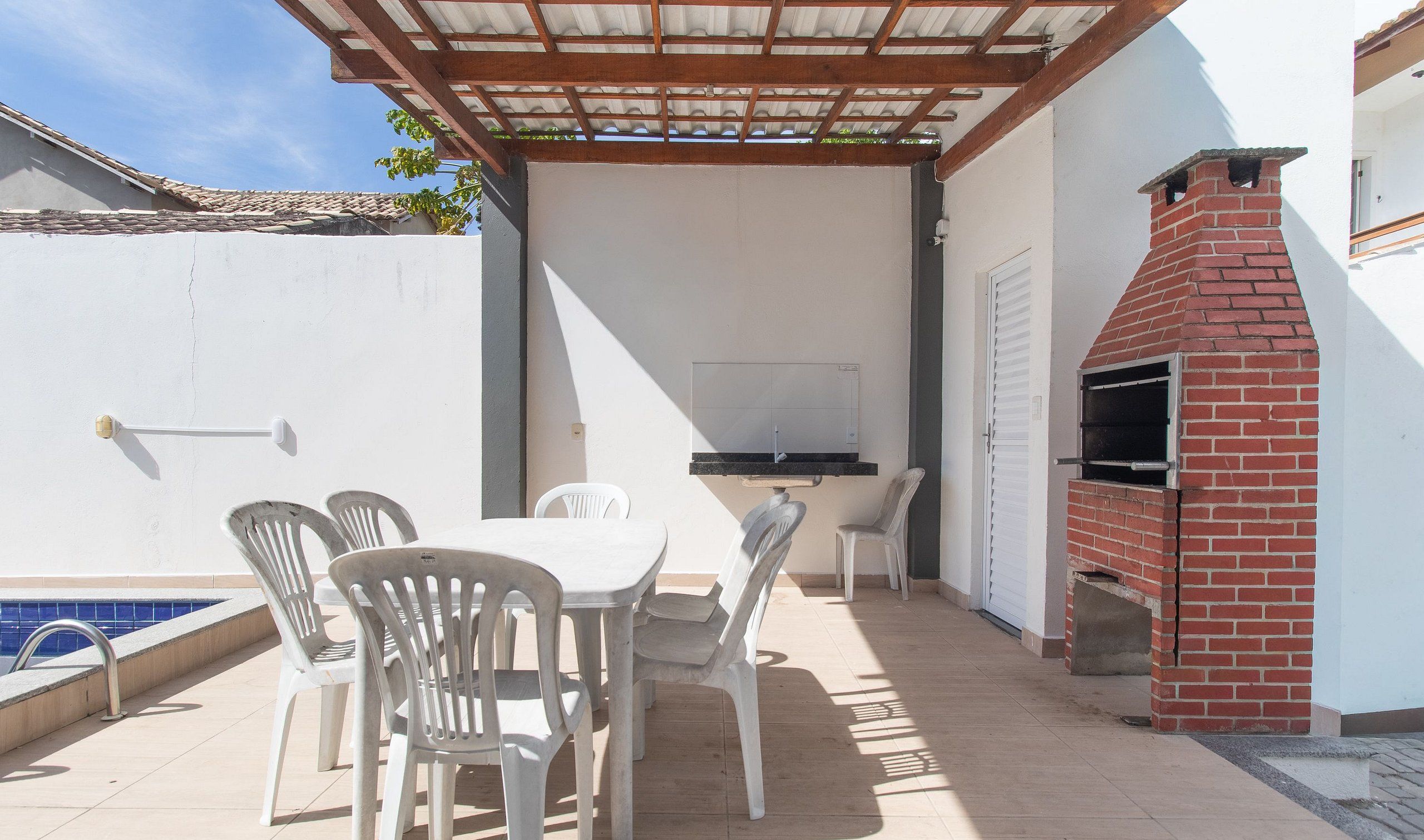 An outdoor patio with a table and chairs, a barbecue grill, and a swimming pool.