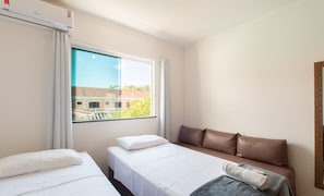 A hotel room with two single beds, a sofa, a large window with a view of a building, and a wall-mounted air conditioner. - Apts in Condominium w/ Pool and Barbecue - Ctys (Porto Seguro)