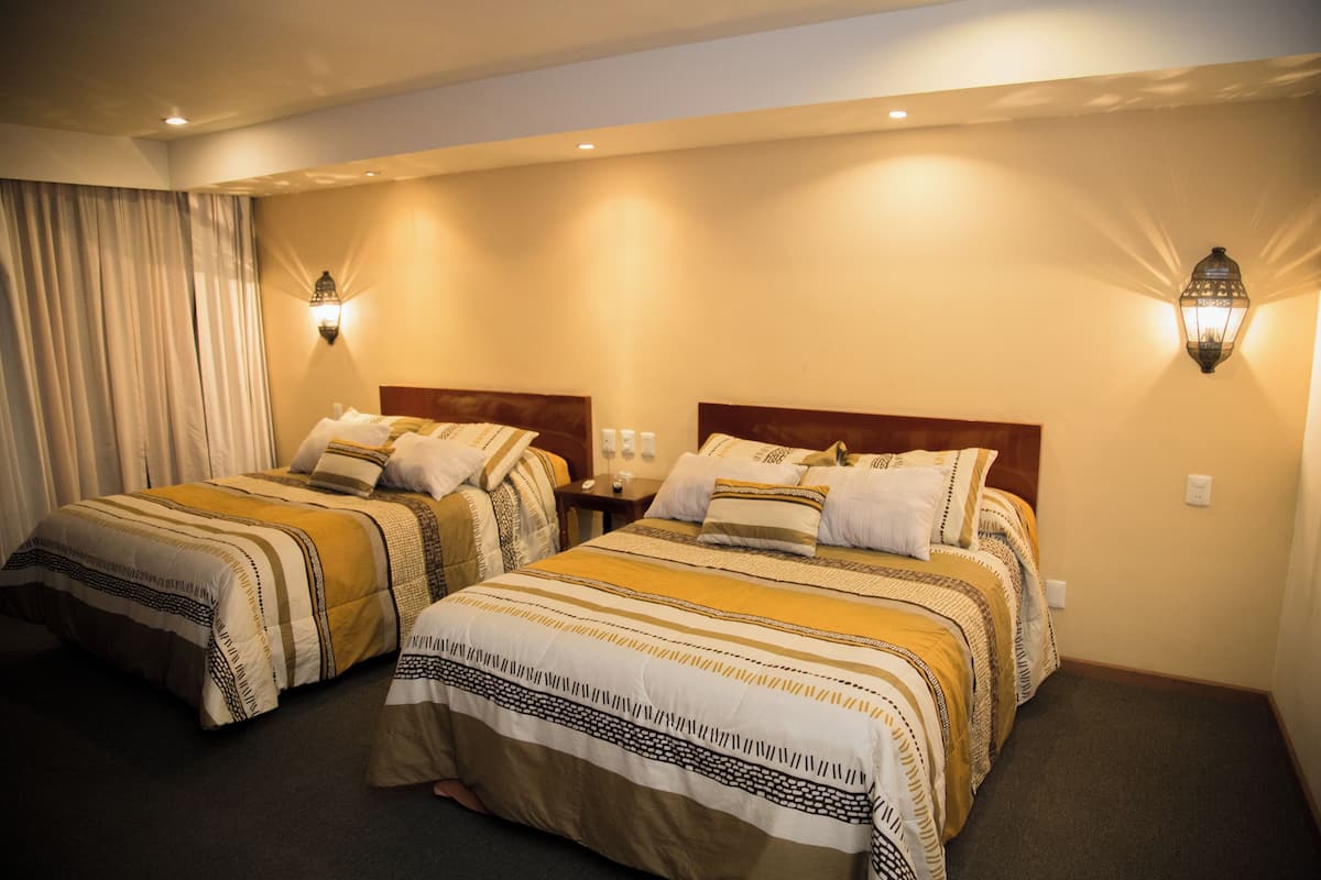 A hotel room with two beds, each with patterned bedding and headboards, and two wall-mounted light fixtures.
