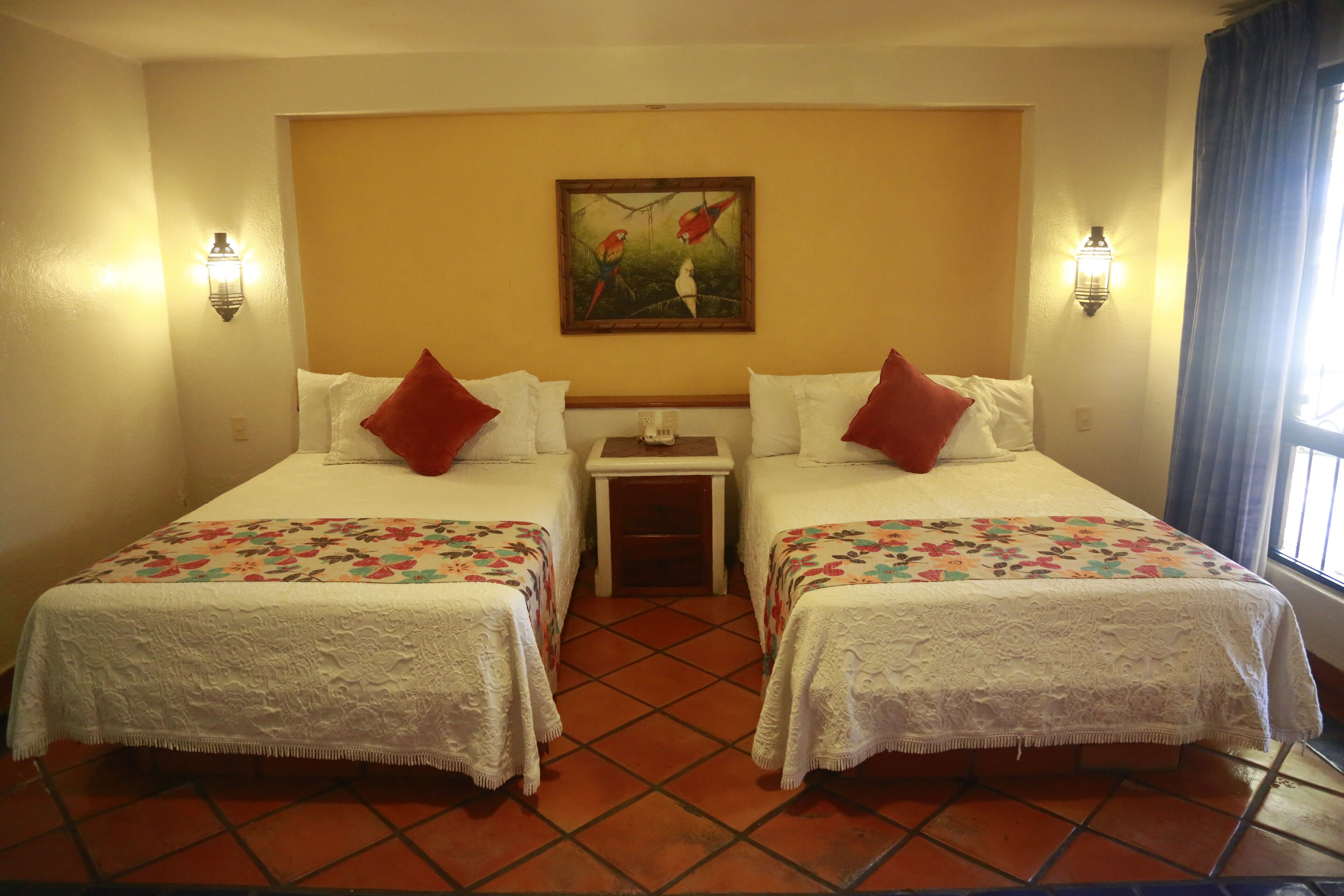 A hotel room with two beds, a nightstand, a painting on the wall, and a window with curtains.
