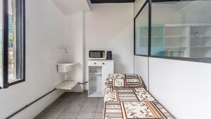 A small, compact room with a bed, a microwave, a sink, and a window offering a view of the outside. - Apto Para 3 Pessoas na Rua Teresa (Petrópolis)