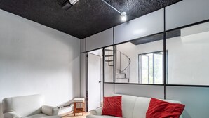A modern living room with a sofa, a chair, and a small table. There is a staircase visible through a glass door. - Apto Para 3 Pessoas na Rua Teresa (Petrópolis)