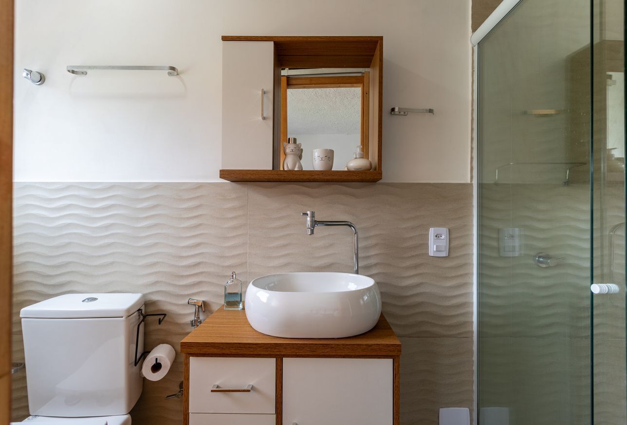 A bathroom with a white toilet, a wooden vanity with a white sink, a mirror above the vanity, and a glass shower enclosure.
