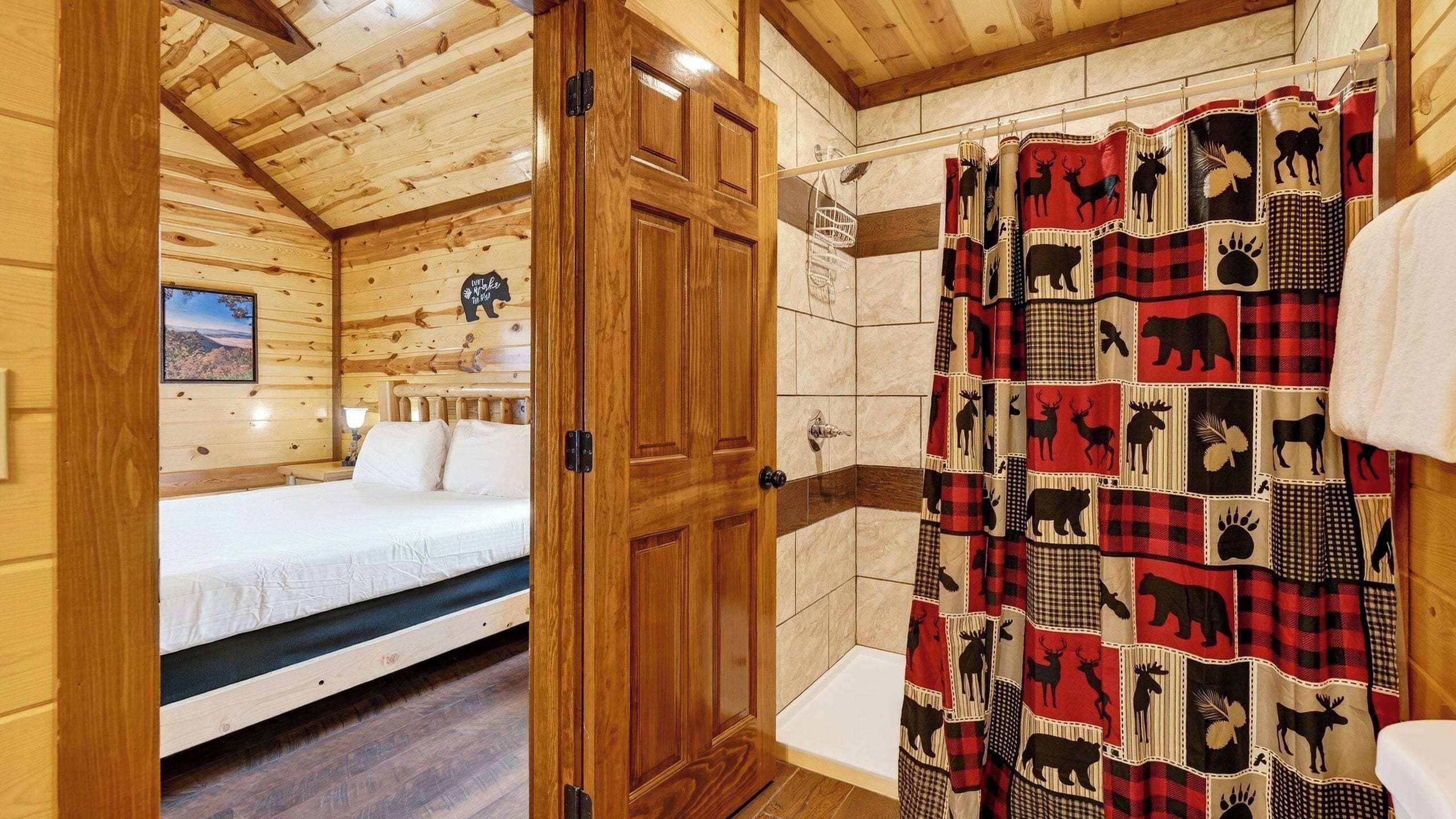L’intérieur d’un chalet en bois comprend un lit, une douche avec un rideau à carreaux rouges et noirs, et une porte en bois.
