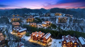 A snow-covered village with multiple wooden cabins, each with a distinct roof design, surrounded by trees and hills. - Green Mountain Lodge by Avantstay Group Retreat Indoor Pool + Hot Tub + Game Room Pigeon Forge + Near Dollywood (Sevierville)