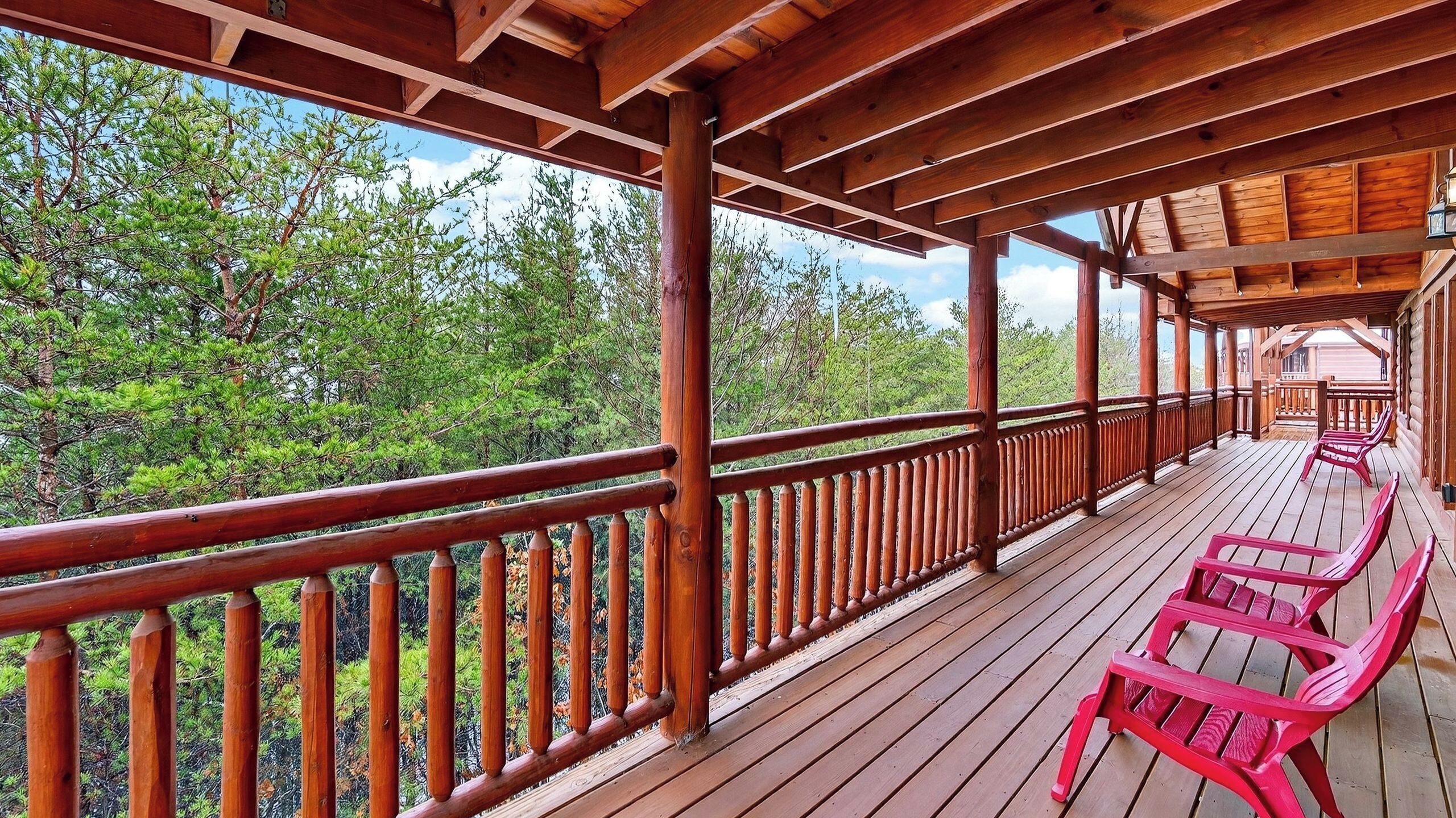 Une terrasse en bois avec une rambarde, des chaises rouges et une vue sur les arbres.
