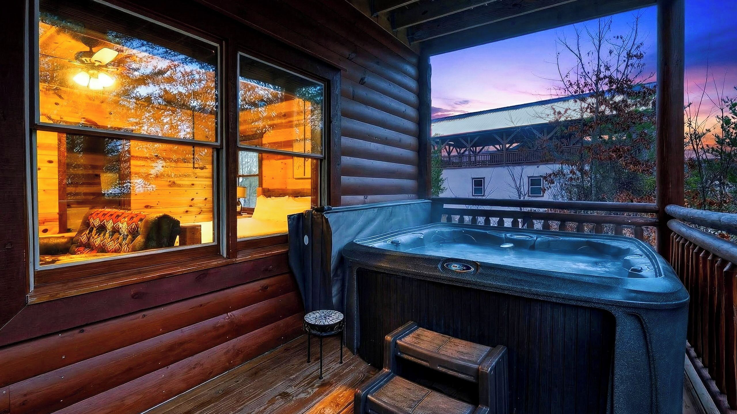 Een houten hut met een jacuzzi, een raam met uitzicht op een zonsondergang en een gezellig interieur.