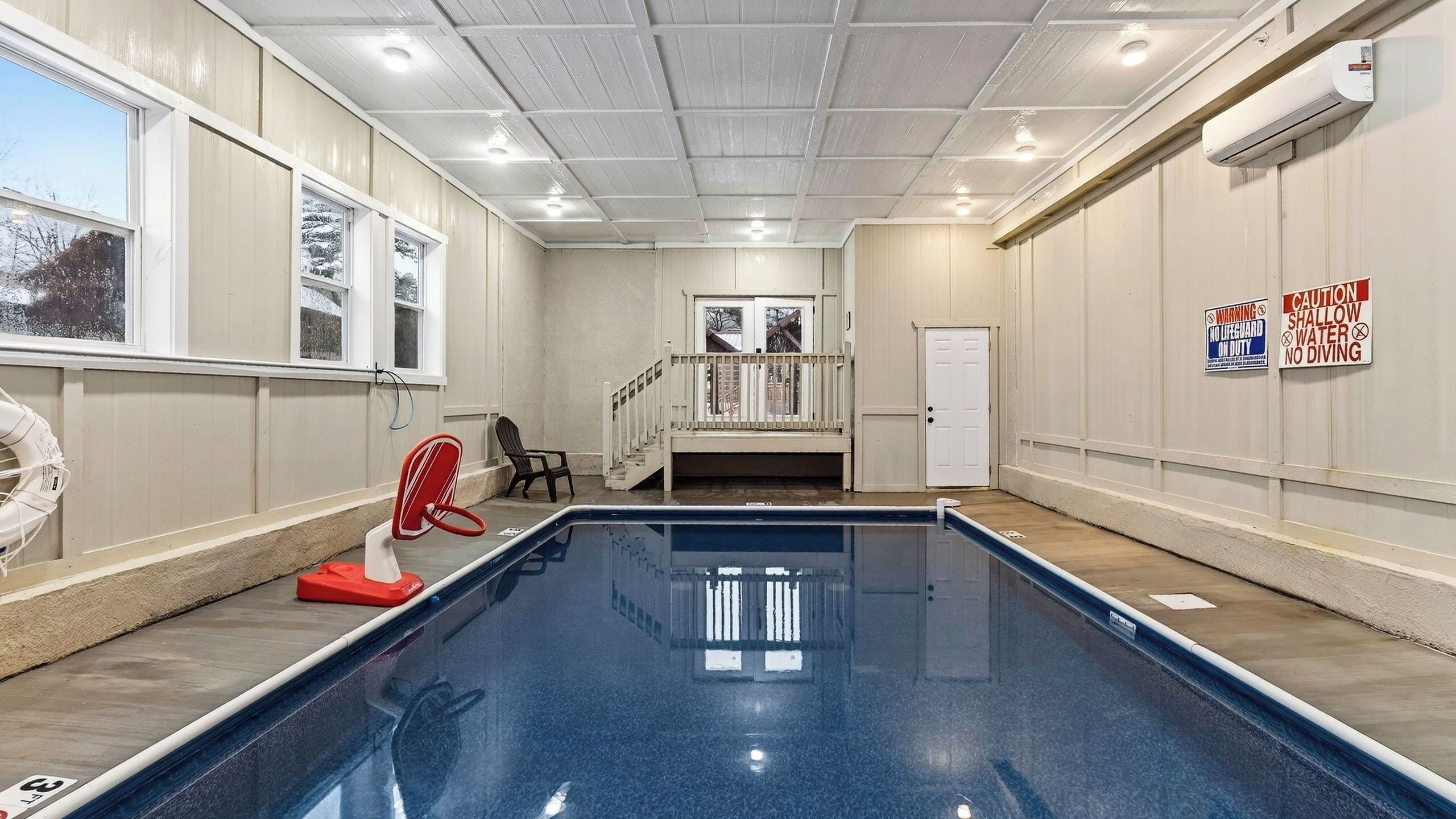An indoor swimming pool with a view of the outside, a lifeguard chair, and safety signs.
