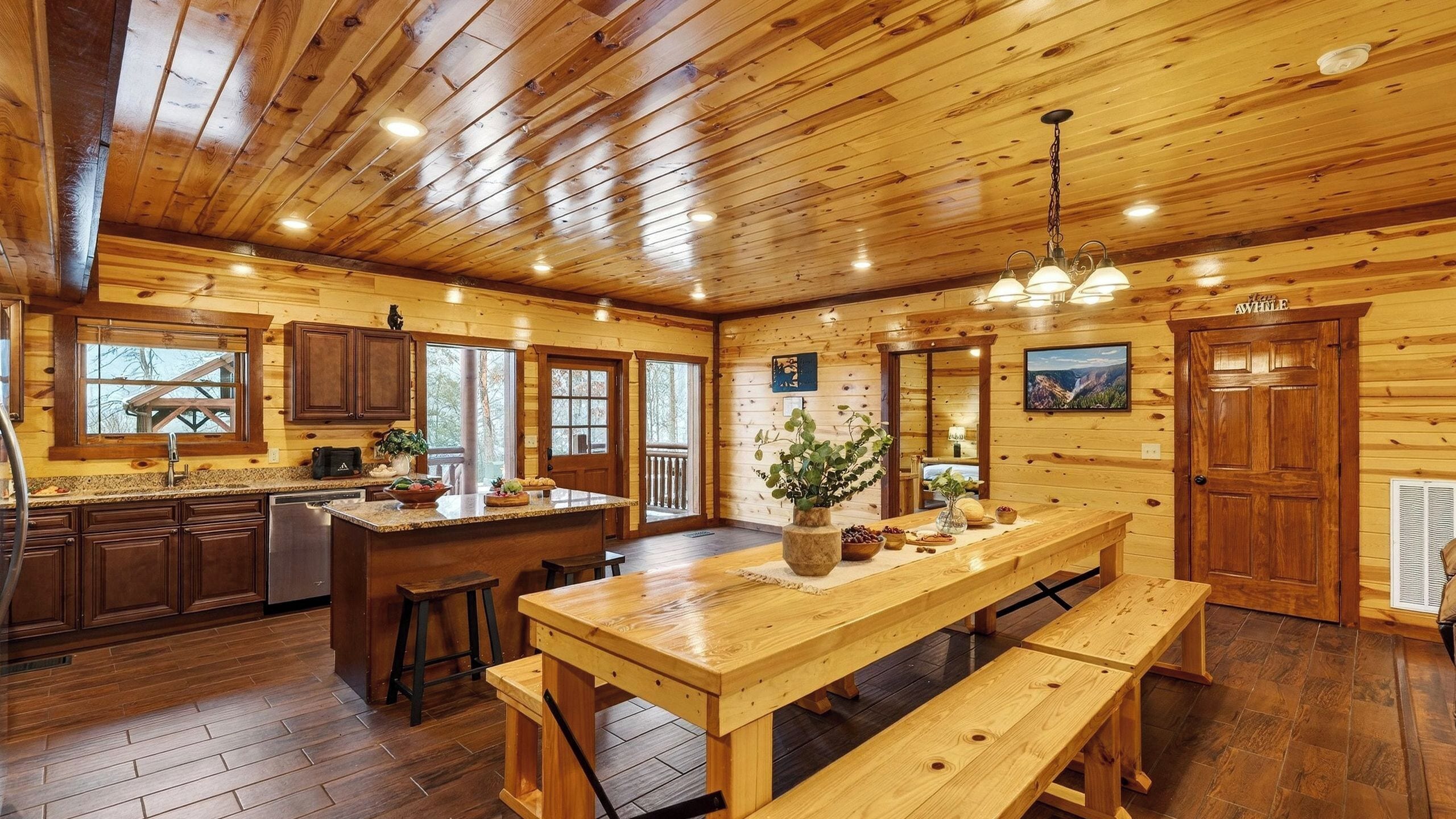 Interior de una cabaña de troncos con cocina, comedor y una gran puerta de madera que dice 'AVILLE'.