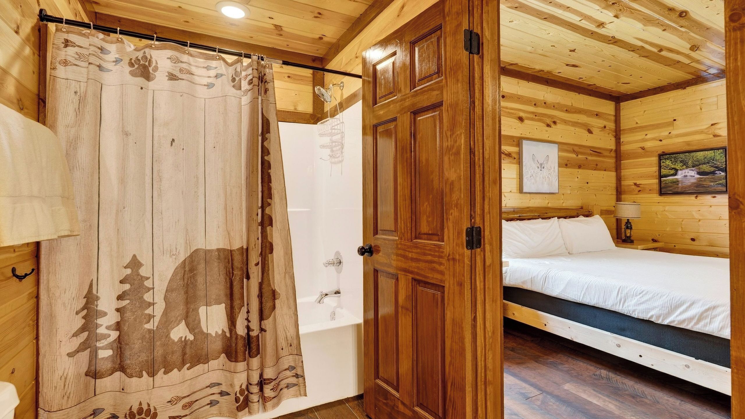 Quarto de cabana de madeira com cama, banheiro com cortina de chuveiro e porta de madeira.