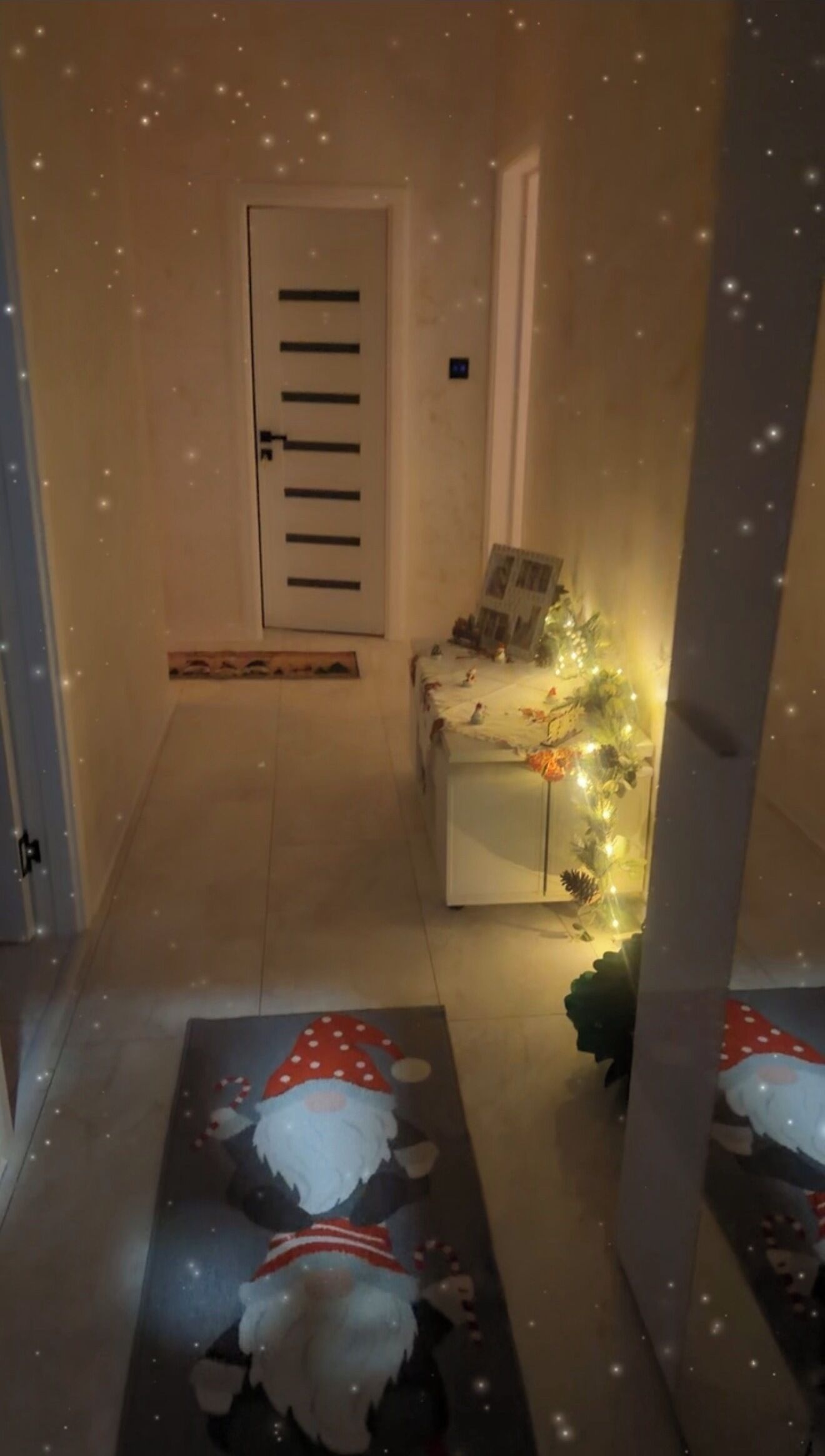 En hall med en dörr, ett litet bord med en växt och en jultomte-dekoration på golvet.