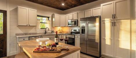 A modern kitchen with white cabinetry, stainless steel appliances, and a wooden island with food and wine.