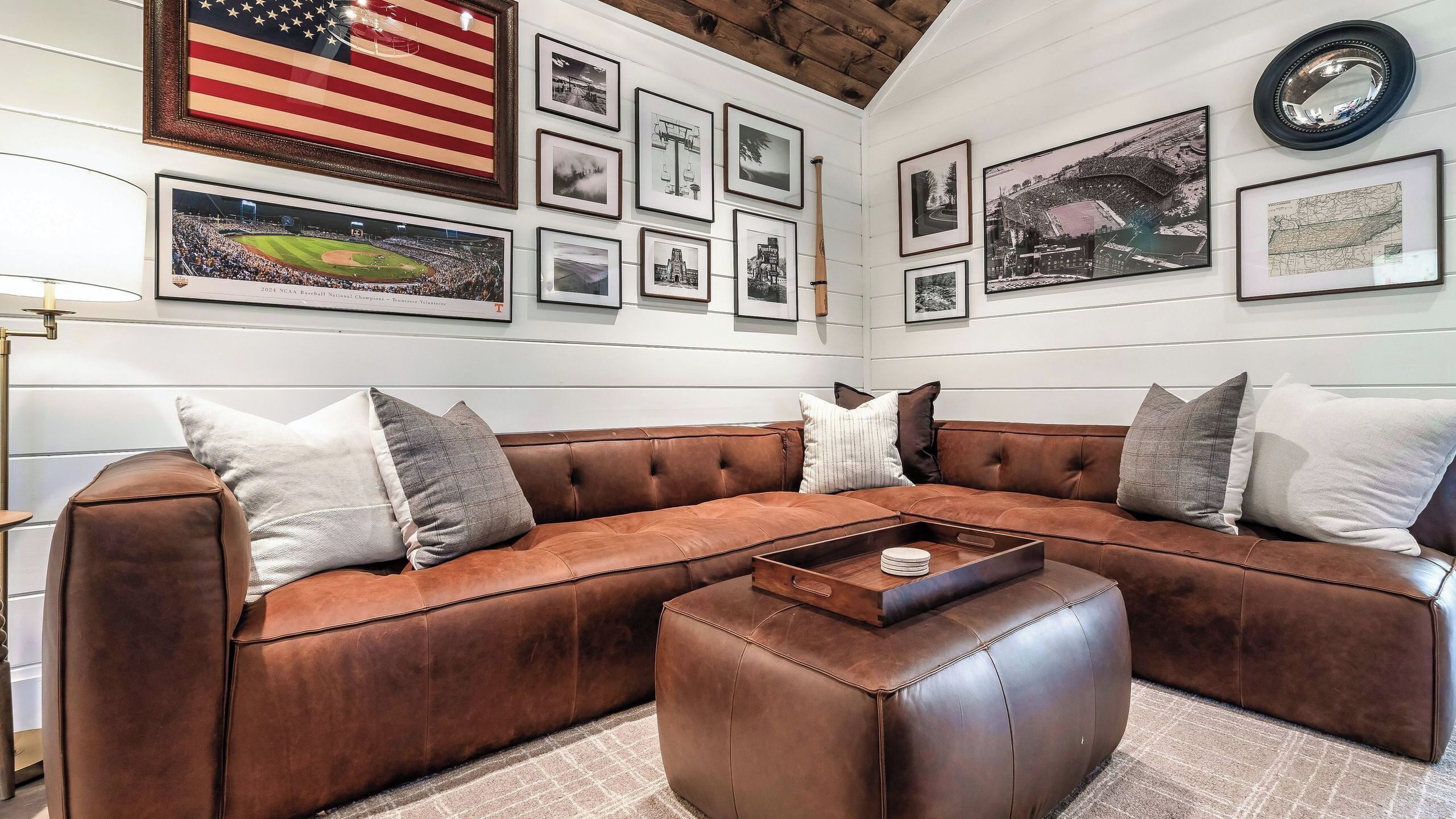 A room with a brown leather sectional sofa, a coffee table, and various framed pictures on the walls.