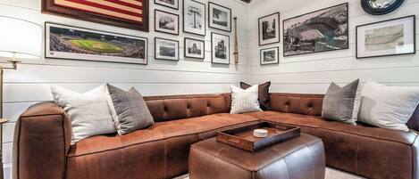 A room with a brown leather sectional sofa, a coffee table, and various framed pictures on the walls.