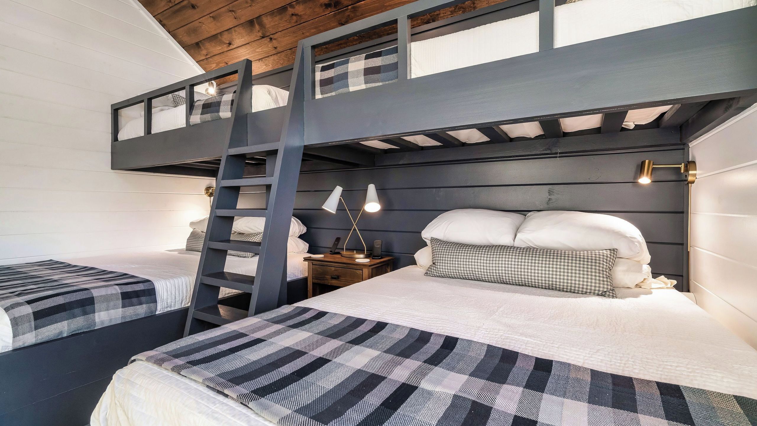 A bunk bed room with a ladder, two bedside tables, and a wall-mounted lamp.