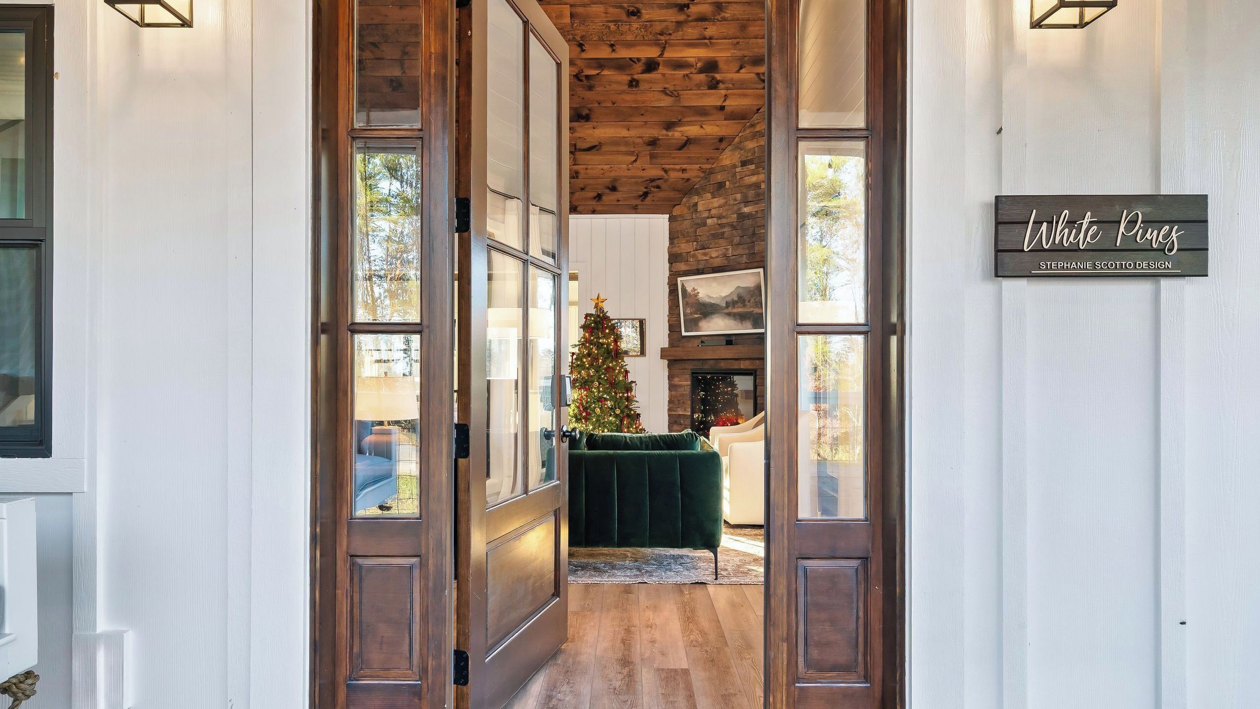 Un interior de madera con un árbol de Navidad, un letrero que dice 'White Pines Stephanie Scotto Design', y vistas a una sala de estar con un sofá verde.