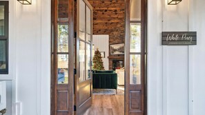 Un intérieur en bois, avec un sapin de Noël, une enseigne indiquant « White Pines Stephanie Scotto Design », et une vue sur un salon doté d’un canapé vert.