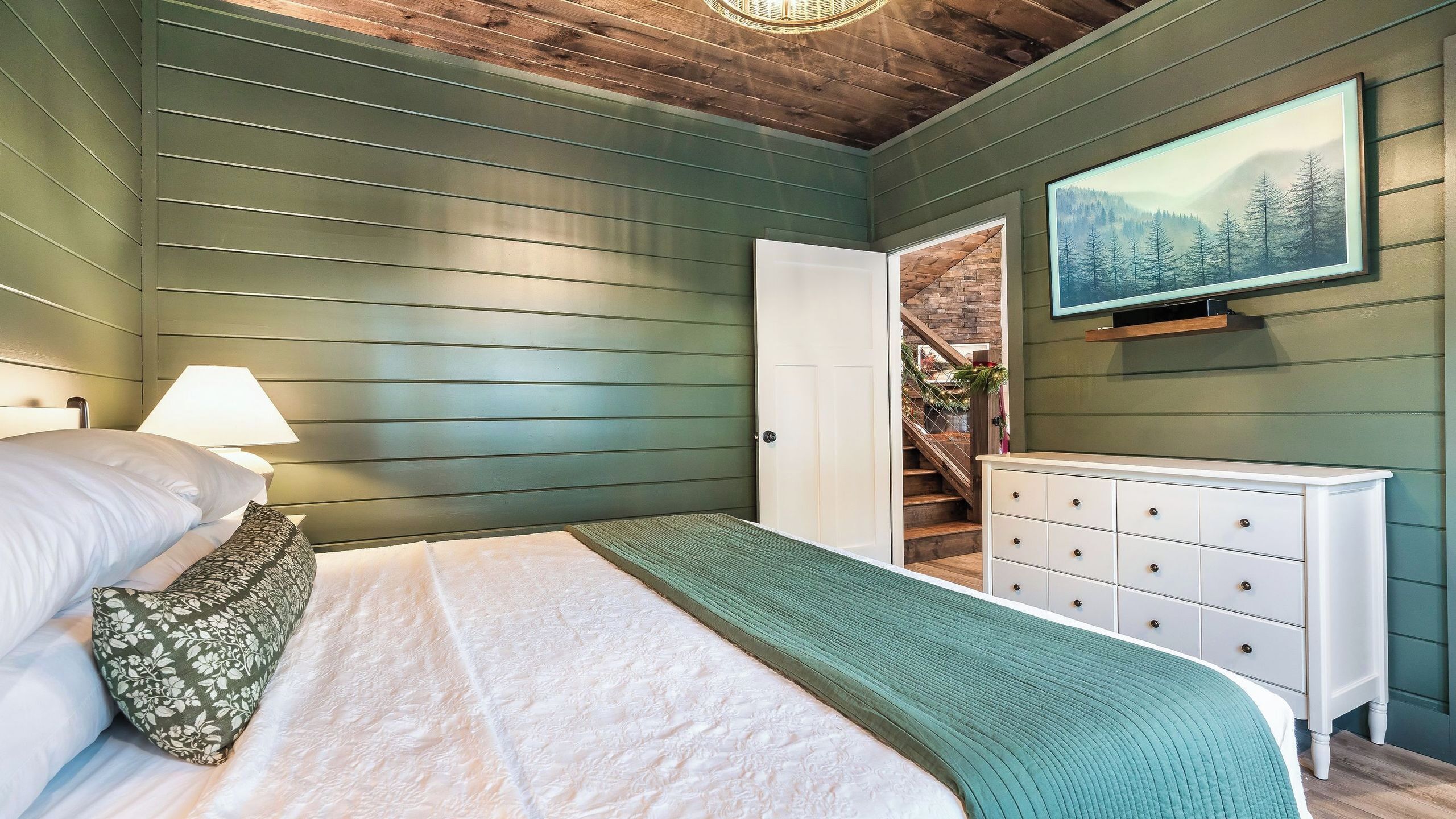 Une chambre à coucher avec un lit, une commode, un tableau et un escalier.