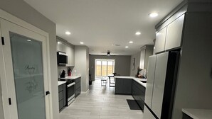 Et moderne køkken med en glasdør mærket 'Pantry', et spiseområde med bord og stole, samt udsigt til en træterrasse.