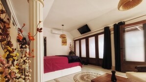 Une chambre à coucher avec un lit, une table en bois, une plante décorative et une grande fenêtre avec des rideaux.