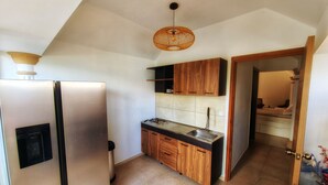 Une cuisine compacte dotée d’un réfrigérateur encastré, de meubles de rangement en bois, d’une cuisinière à gaz et d’un luminaire suspendu.