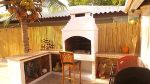 Un espace cuisine extérieur doté d’un plan de travail en pierre, d’une chaise en bois, d’un barbecue et d’un four en briques.