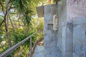 A stone shower enclosure with a metal handrail, surrounded by greenery. - Stunning Ocean View at Kahakai House in Guiones (Nosara)