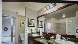 A bathroom with a large mirror, two sinks, a toilet, and framed pictures on the wall.