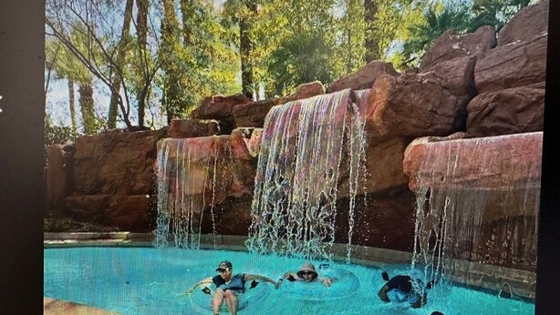 A pool area with a waterfall feature, surrounded by trees and rocky formations.