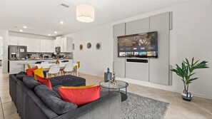 Un salon moderne avec un canapé d’angle gris, une table basse en verre et un téléviseur à écran plat fixé au mur.
