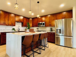 Una cocina moderna con armarios de madera, un refrigerador de acero inoxidable y una encimera de mármol.