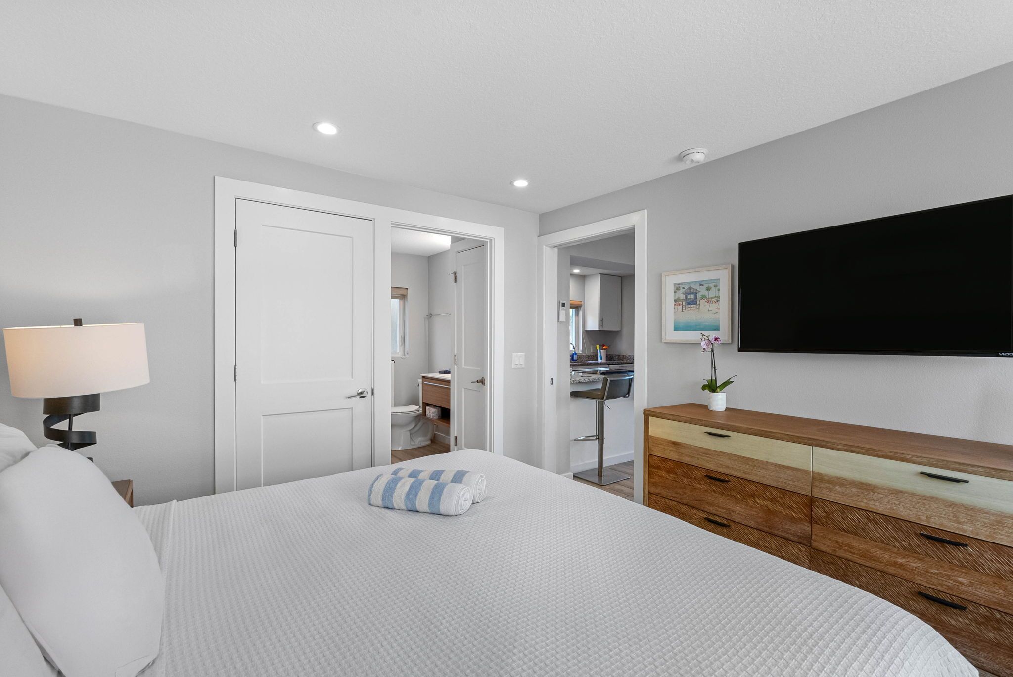 Een moderne slaapkamer met een bed, een bedlamp, een dressoir, een televisie en een badkamer die door een open deur zichtbaar is.