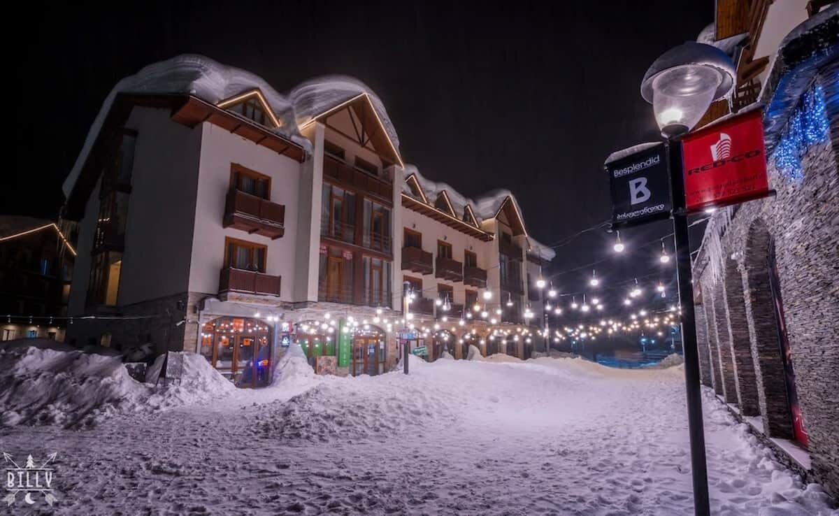 Una strada innevata con edifici e un cartello con la scritta 'B' hotel.