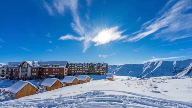 Eine Lodge mit mehreren Holzhütten und einem großen Gebäude mit Balkonen, vor einer verschneiten Berglandschaft.