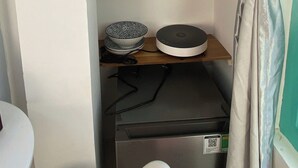 Eine kleine Küche mit Regalen, auf denen Töpfe, Tassen, ein Wasserkocher und eine Kaffeemaschine stehen.