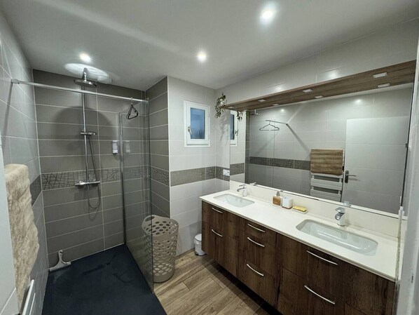 Un baño moderno con ducha, tocador y un espejo grande.