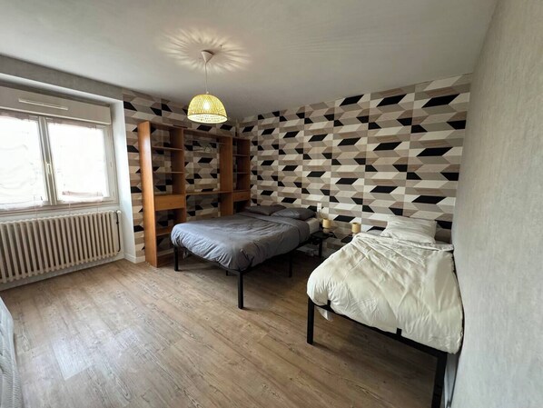 Un dormitorio con dos camas, una estantería de madera y una pared con diseño geométrico.