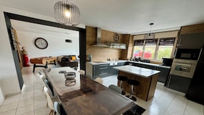 Cozinha moderna com ilha central, área de jantar com mesa comprida e sala de estar com sofá e mesa de centro.