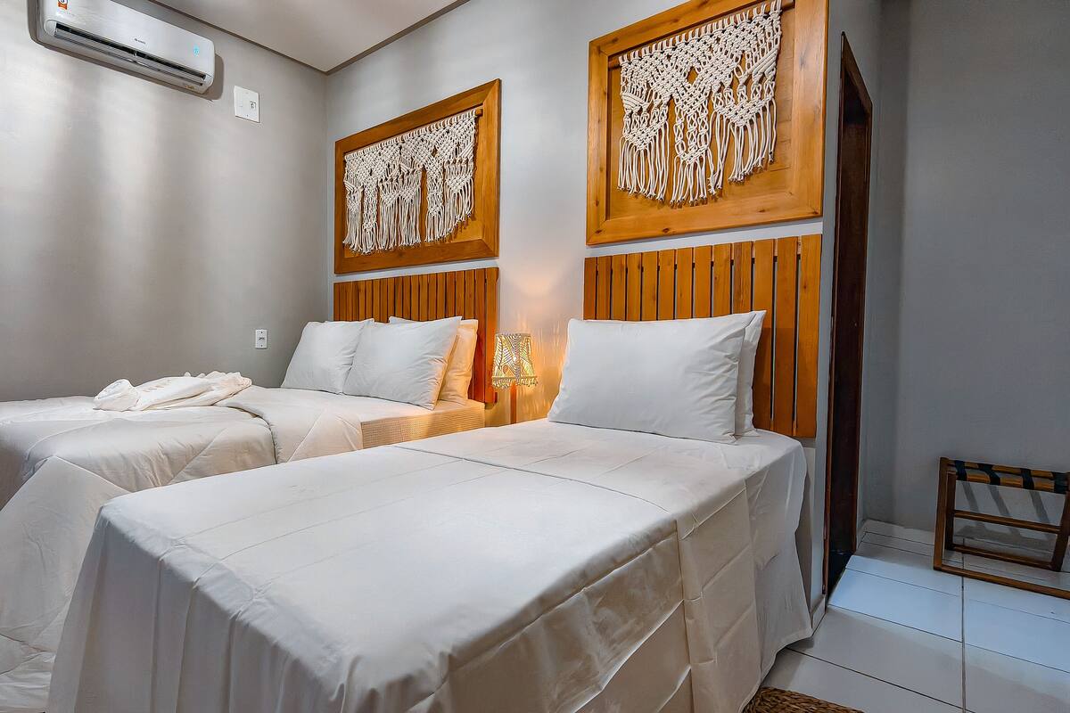 Habitación de hotel con dos camas, un cabecero de madera, una decoración de pared de macramé y una pequeña silla de madera.