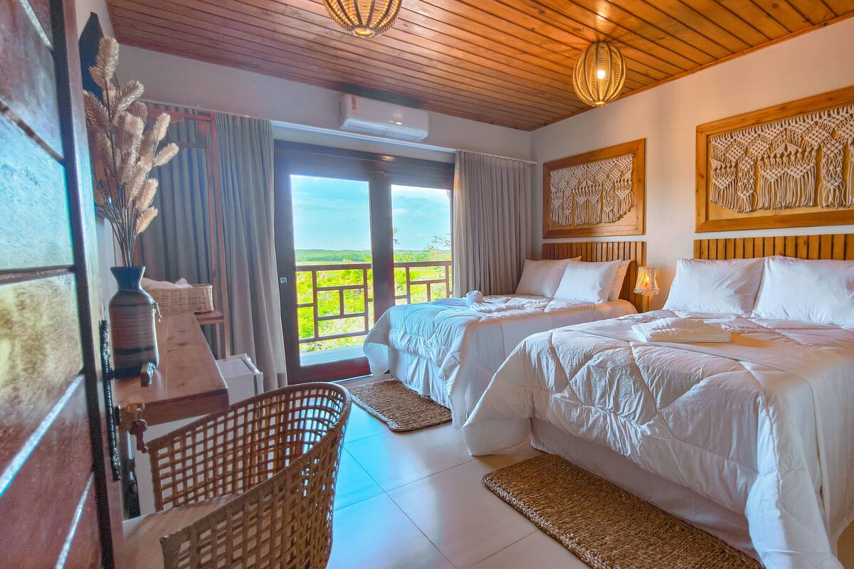 Habitación de hotel con dos camas, techo de madera, un ventanal con vistas y decoración de macramé en la pared.